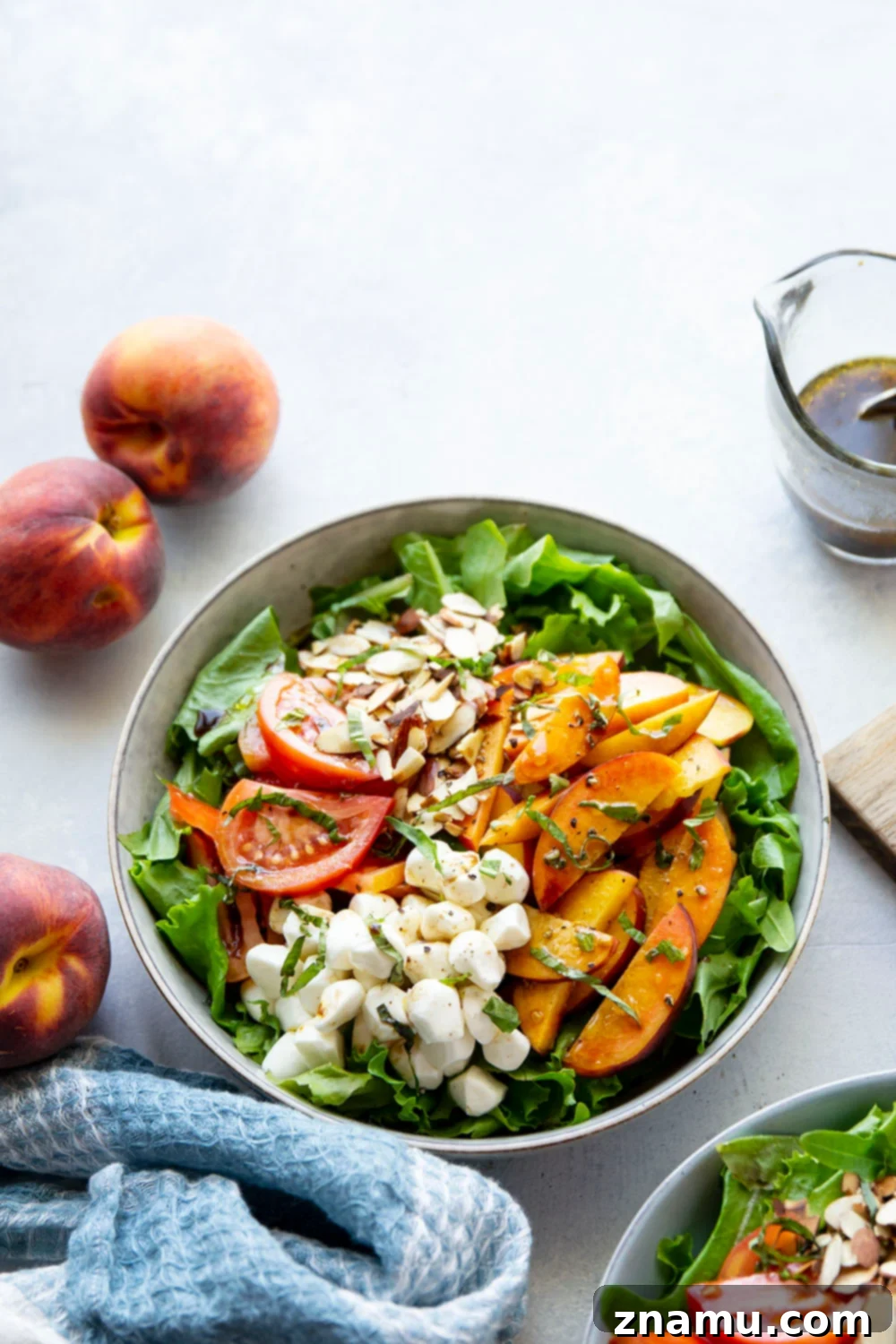 Sun-Drenched Peach Caprese 5 Assortment of fresh ingredients for caprese salad, including whole peaches, colorful tomatoes, a bowl of mozzarella pearls, and fresh basil leaves, on a light background.