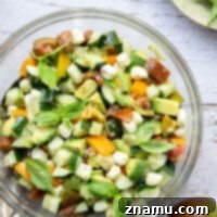A vibrant Italian Tomato Cucumber Salad, featuring fresh tomatoes, creamy avocados, crisp cucumbers, and soft mozzarella pearls, generously tossed in a flavorful homemade Italian vinaigrette.