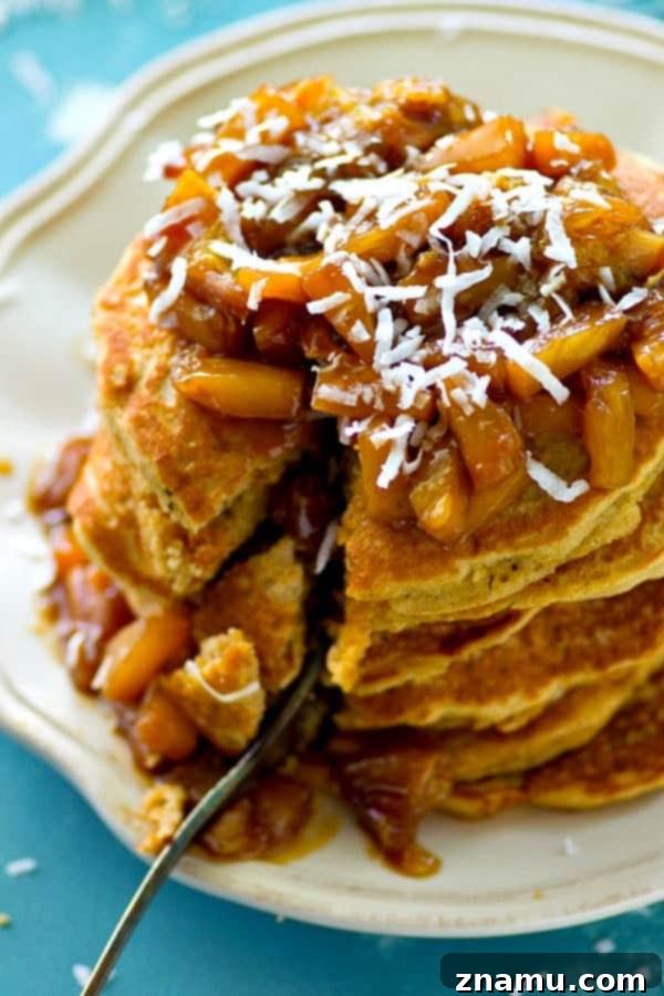 Coconut Cloud Pancakes with Zesty Orange-Pineapple Compote 6 Delicious coconut pancakes generously topped with a rich orange pineapple compote, garnished with shredded coconut.