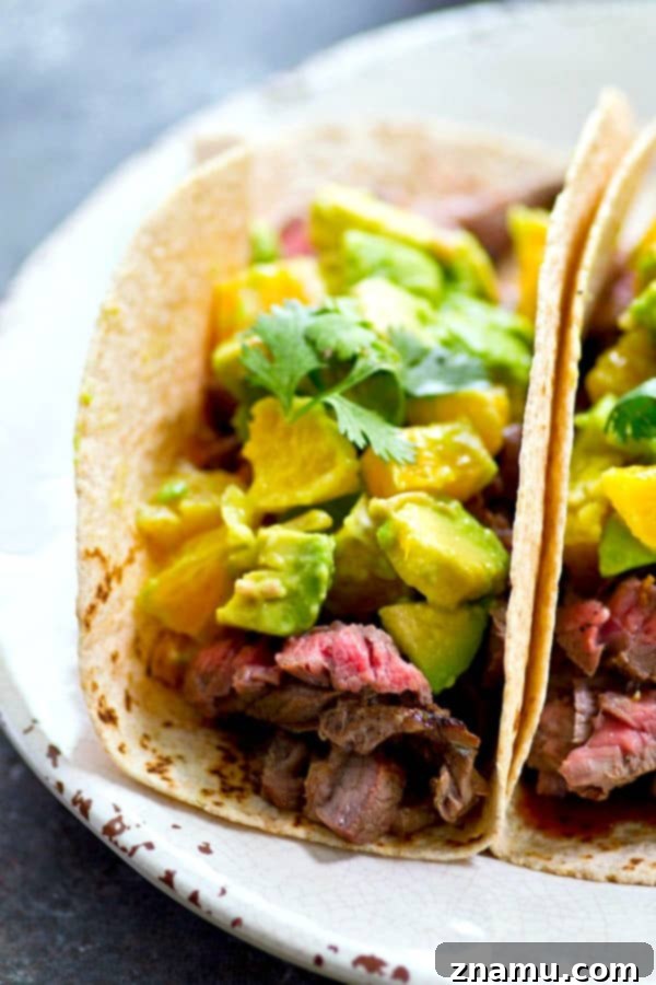 Perfectly grilled flank steak tacos topped with vibrant orange avocado salsa, ready to be enjoyed.