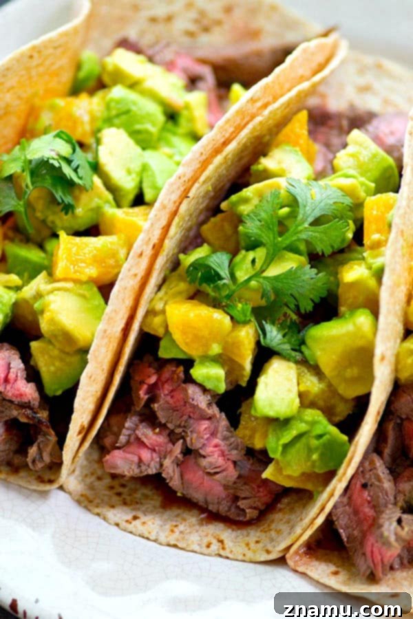 Close-up of a loaded steak taco showcasing the juicy flank steak and colorful orange avocado salsa.