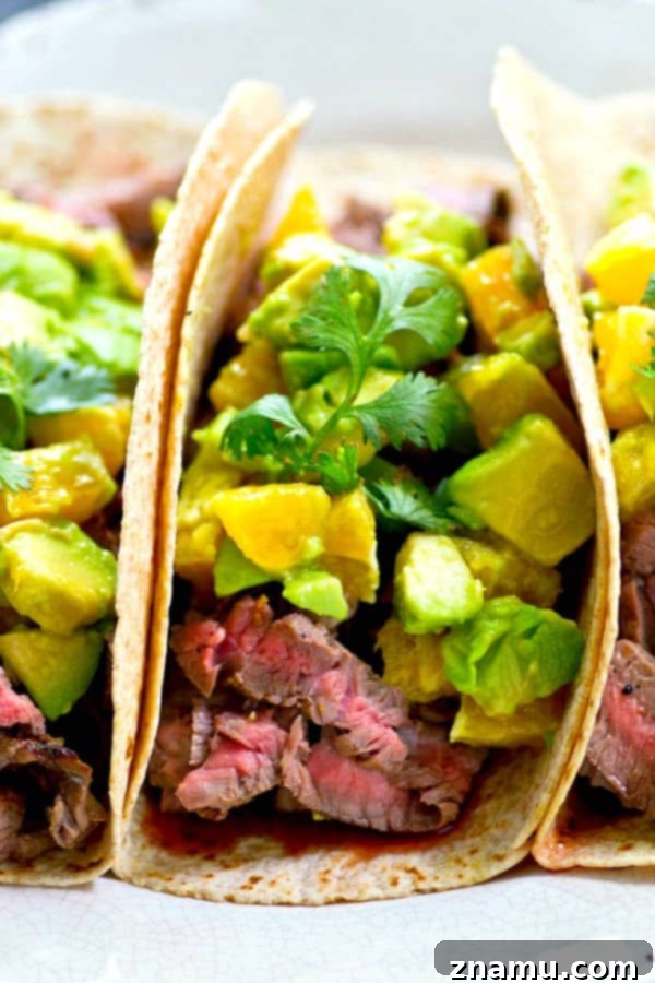 Prepared citrus grilled steak tacos topped with orange avocado salsa, served on a rustic wooden board.