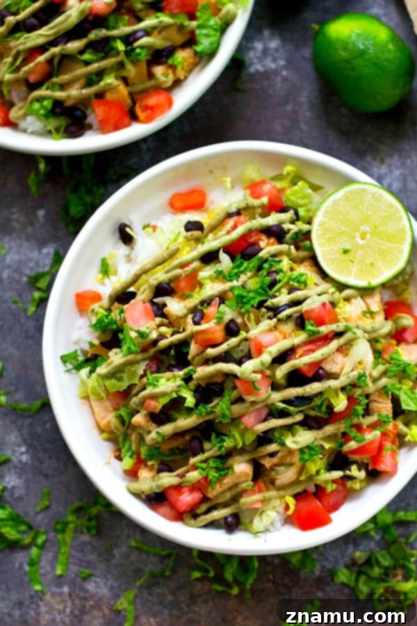 A colorful and generously portioned Chipotle Lime Chicken Burrito Bowl, featuring fluffy white rice, perfectly seasoned chicken, and a drizzle of creamy avocado crema.