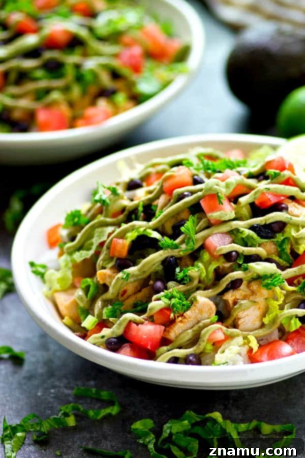 Close-up of a burrito bowl showcasing tender chipotle lime chicken, a bed of white rice, black beans, diced tomatoes, and a generous dollop of avocado crema.