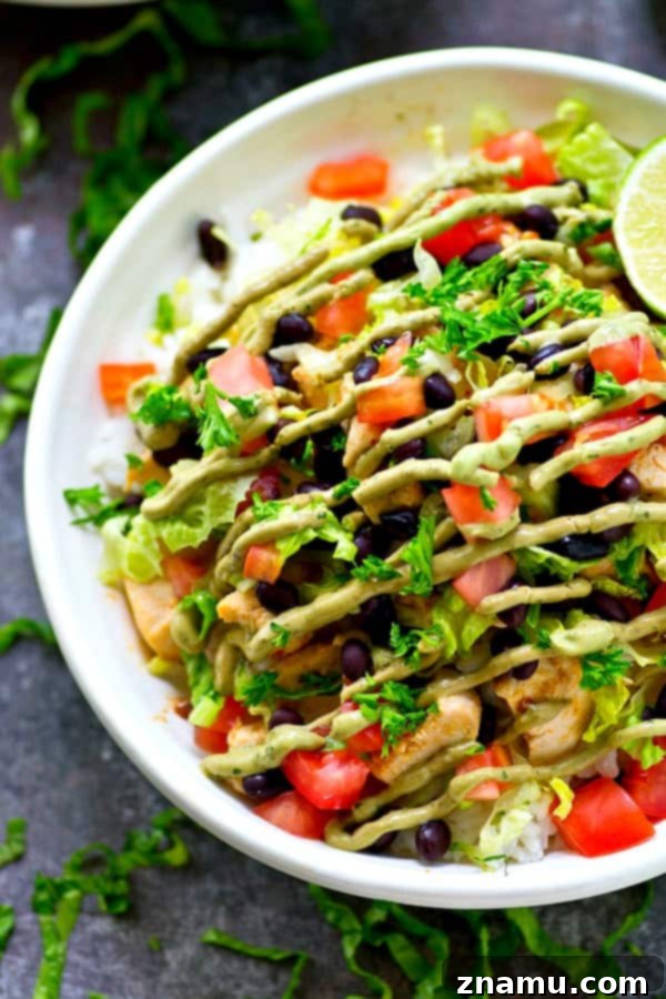 Overhead view of a Chipotle Lime Chicken Burrito Bowl being assembled, with various fresh toppings like lettuce, beans, and tomatoes laid out alongside the cooked chicken and rice.