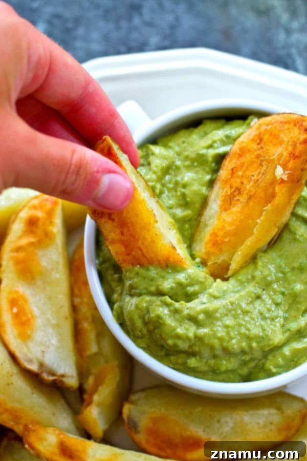 Golden Crispy Wedges with Creamy Poblano Avocado Ranch 6 Close-up of a crispy potato wedge being dipped into a bowl of green poblano avocado ranch dip