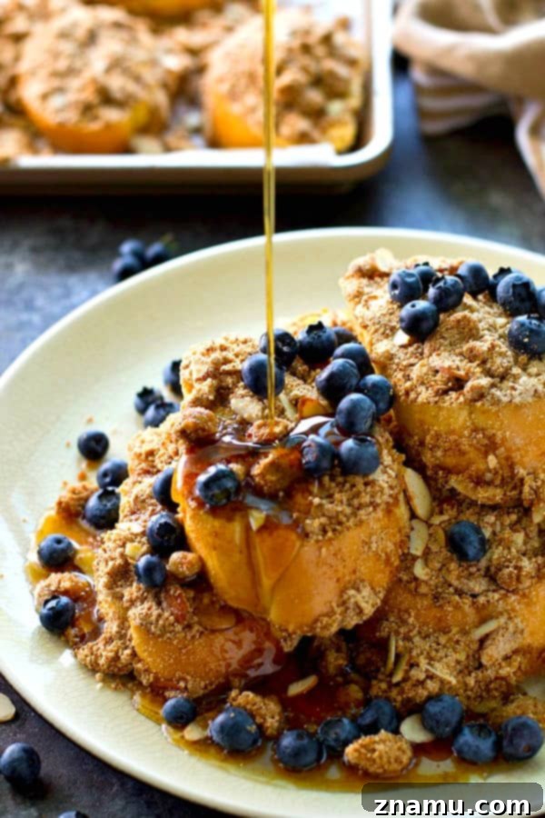 Decadent Baked Almond Streusel French Toast 6 Baked almond streusel French toast served with fresh berries and maple syrup on a plate.