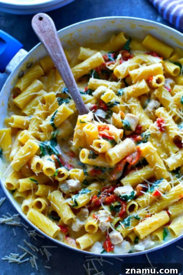 Tuscan Chicken Alfredo with Sun-Dried Tomatoes and Spinach 5 A serving of One-Pot Sun-Dried Tomato Spinach Chicken Pasta Alfredo in a bowl, garnished with fresh parsley and grated Parmesan cheese.
