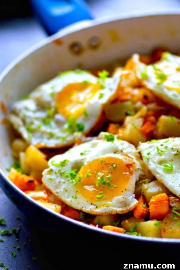Vibrant Veggie Hash & Golden Yolks 5 A serving of rainbow vegetable hash topped with two fried eggs, garnished with fresh herbs.