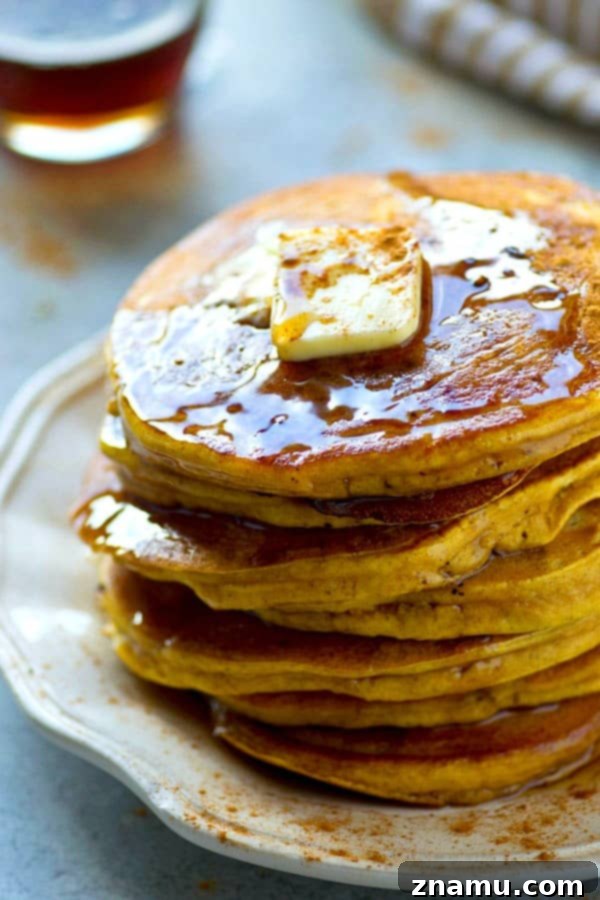 Close-up of a stack of golden-brown pumpkin chai spice pancakes with melted butter and syrup, showing their light and airy texture.