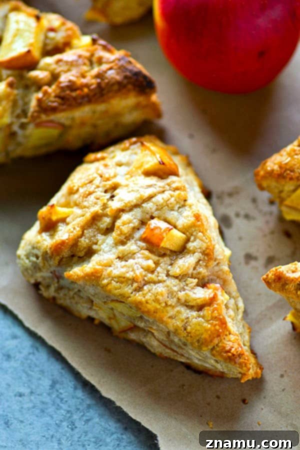 Maple Apple Cream Cheese Scones 5 A stack of golden, warm Maple Cream Cheese Apple Scones on a rustic wooden board, garnished with fresh apple slices and a drizzle of maple syrup, evoking a cozy fall feeling.