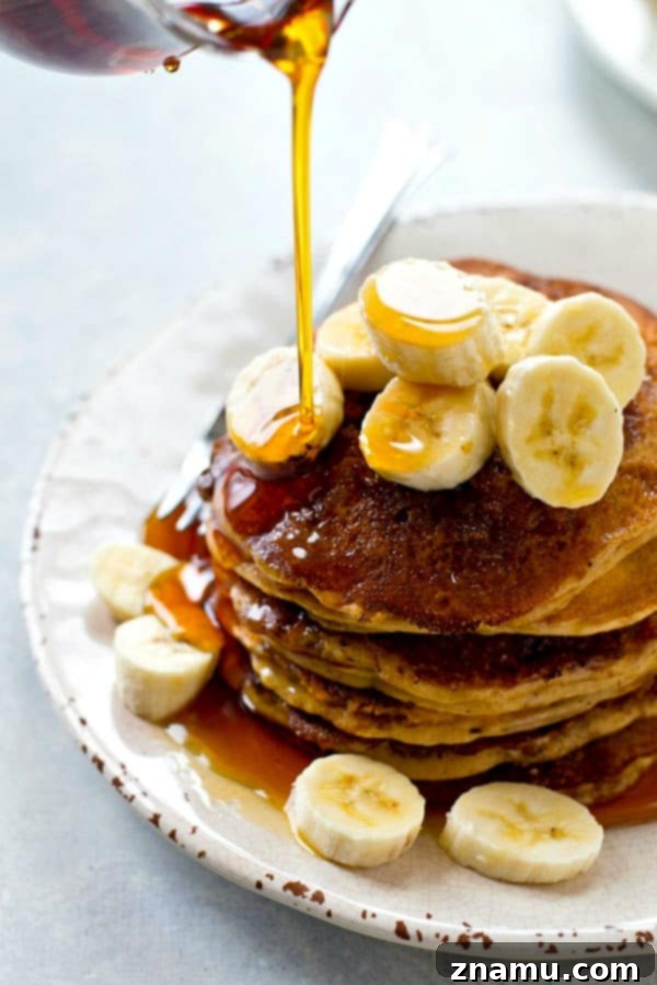 Stack of cinnamon crunch banana buttermilk pancakes with a drizzle of syrup and banana slices