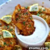 Golden-Crisp Lemon Parmesan Oven-Fried Chicken Tenders 7 A single crispy lemon Parmesan oven-fried chicken tender on a small plate, garnished with fresh herbs.