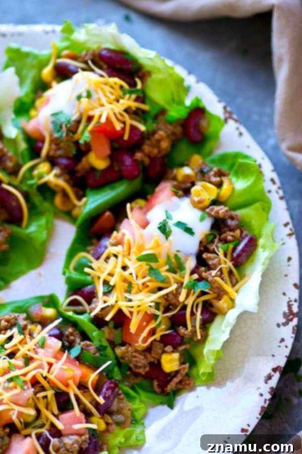 Bold Beef Taco Lettuce Bundles 4 Three perfectly assembled healthy beef taco lettuce wraps on a rustic wooden board, garnished with fresh cilantro, ready to be enjoyed.