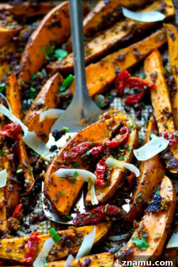 Tangy Pesto Roasted Sweet Potato Wedges 2 Golden roasted sweet potato wedges coated in rich sun-dried tomato pesto, garnished with fresh Parmesan shavings, served hot on a baking sheet.