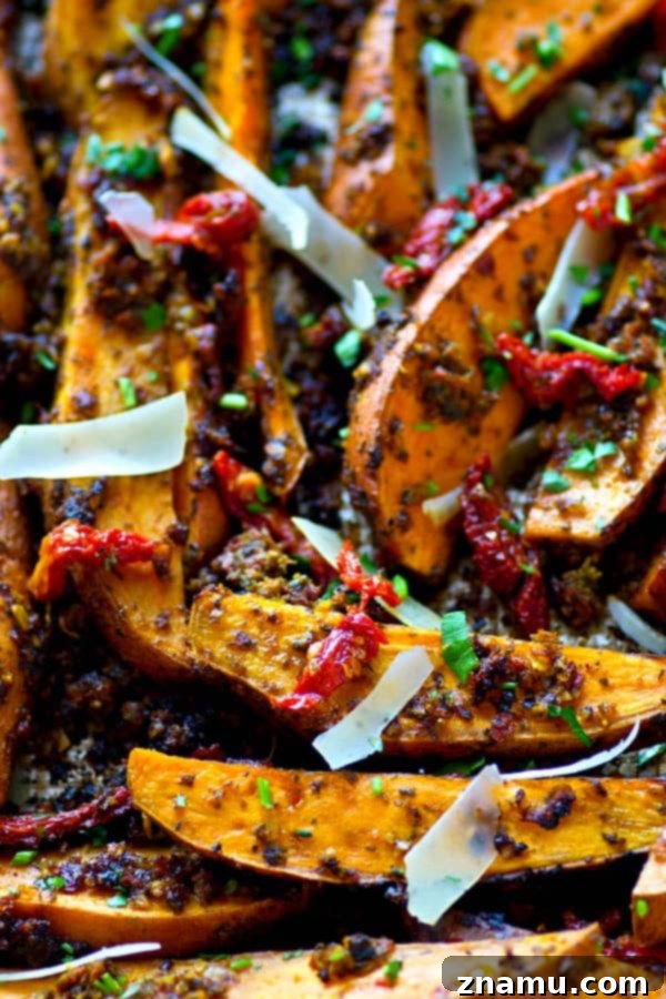 Tangy Pesto Roasted Sweet Potato Wedges 3 Close-up of crispy sweet potato wedges generously coated in a bright red sun-dried tomato pesto, dusted with Parmesan cheese, on a baking sheet.
