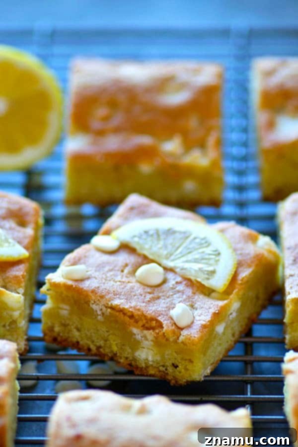 A stack of golden-brown White Chocolate Lemon Blondies on a wire rack, with a scattering of extra white chocolate chips.