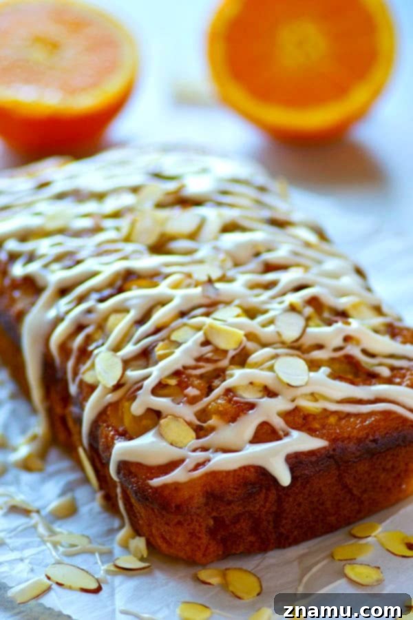 Zesty Orange Almond Glaze Loaf 3 Close-up shot of the Glazed Almond Orange Quick Bread, highlighting the glistening orange glaze and scattered toasted almond slivers on top.
