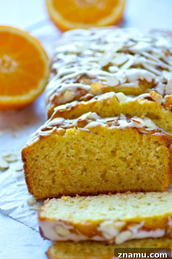 Zesty Orange Almond Glaze Loaf 5 A slice of Glazed Almond Orange Quick Bread on a white plate, ready to be enjoyed, with more of the loaf in the background.
