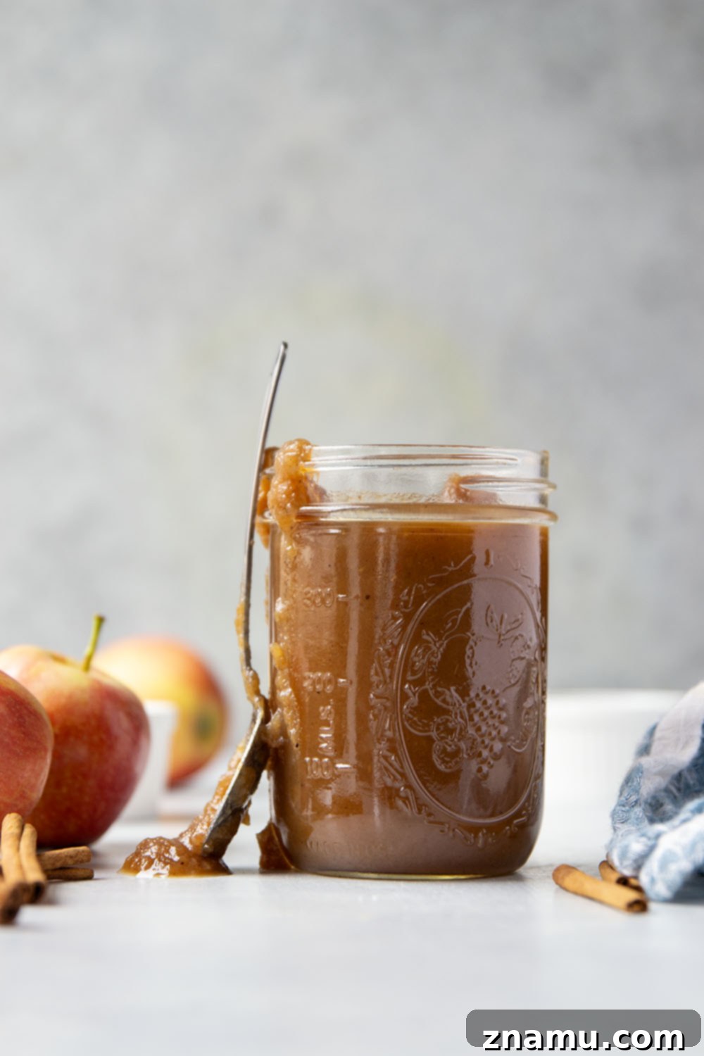 Homemade Slow Cooker Apple Butter 2 A close-up shot of rich, golden slow cooker apple butter in a jar, surrounded by fresh apples and cinnamon sticks, highlighting its smooth texture and inviting color.