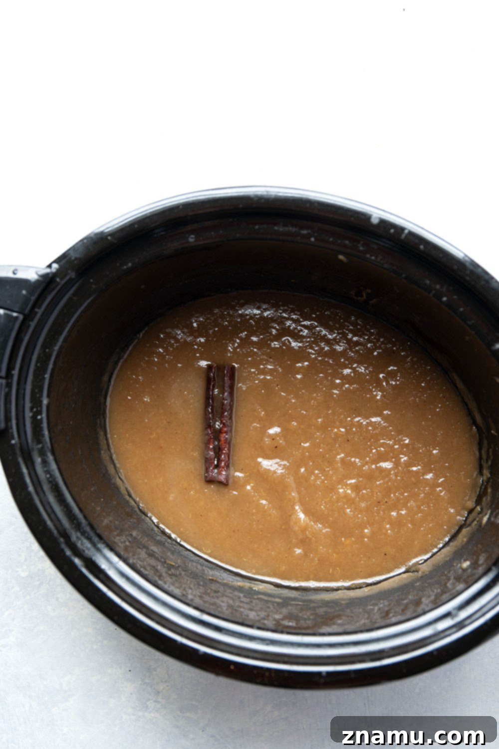 Homemade Slow Cooker Apple Butter 4 Close-up of apples, whole cinnamon sticks, and star anise arranged around a measuring spoon with ground cloves, highlighting the key ingredients for slow cooker apple butter.