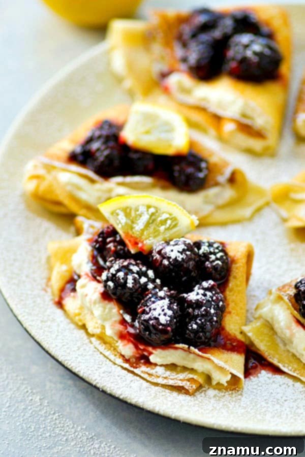 Close-up of freshly made crepes filled with lemon cream cheese and drizzled with vibrant blackberry sauce