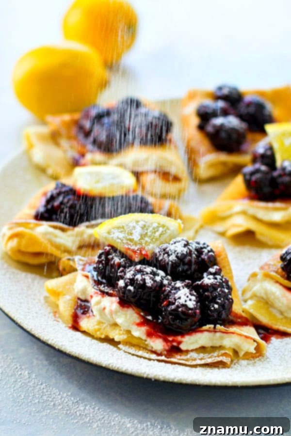 Plate of folded Blackberry Lemon Cream Cheese Crepes, generously topped with fresh blackberries and powdered sugar
