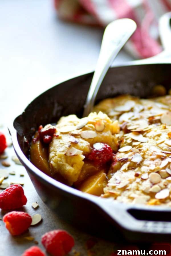 Rustic Skillet Raspberry Almond Peach Cobbler ready to serve, with a scoop of vanilla ice cream melting on top