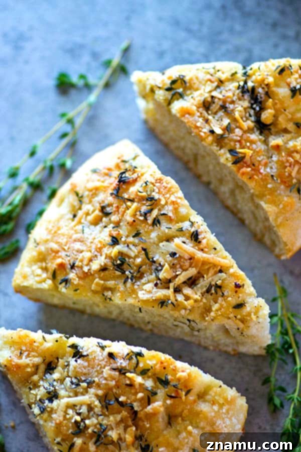 Effortless Overnight Parmesan Herb Focaccia 3 Close-up of the rustic, dimpled surface of a homemade Parmesan Herb Focaccia, showing the melted cheese and fragrant herbs embedded in the golden crust.