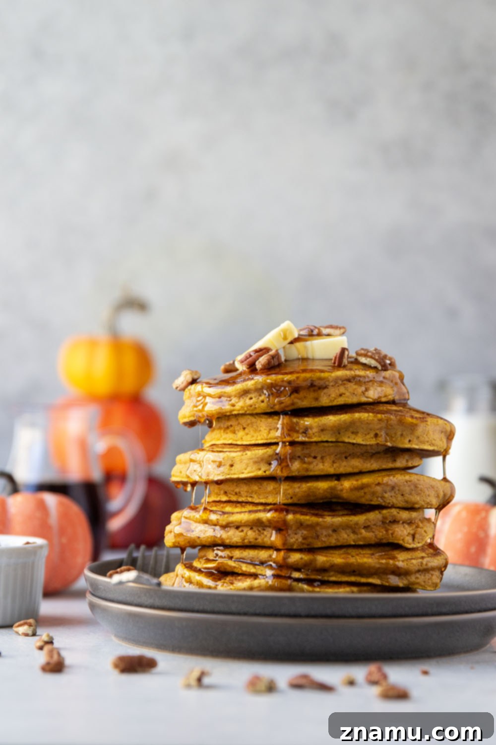 Warm Spiced Pumpkin Stacks 6 A delicious stack of pumpkin spice pancakes generously topped with butter, pecans, and flowing maple syrup, ready to be enjoyed.