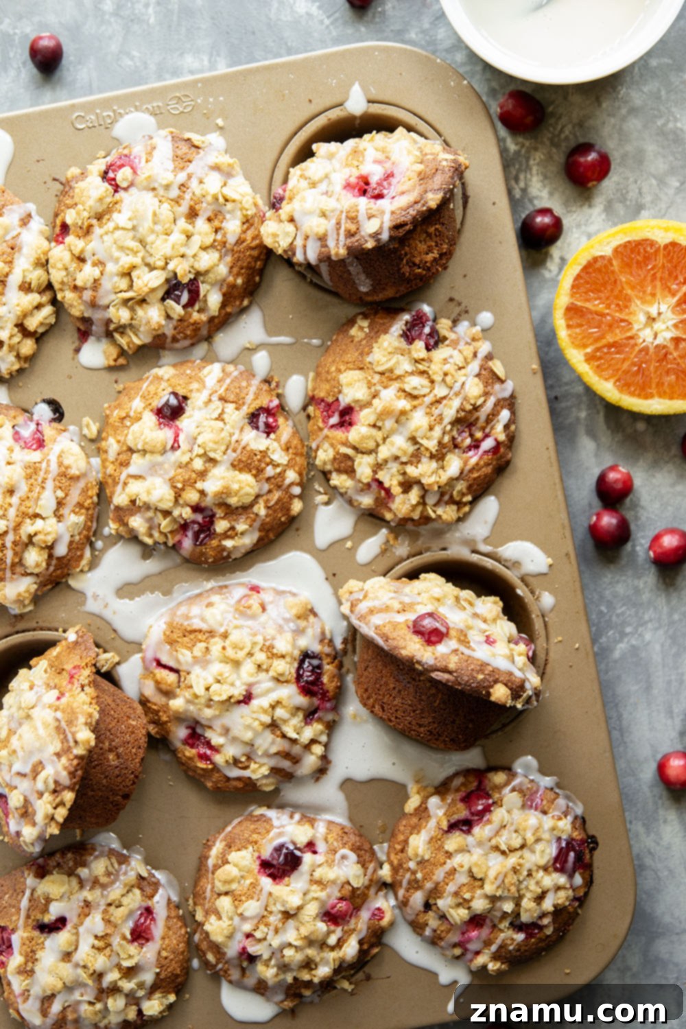 Wholesome Cranberry Oat Muffins 6 Several cranberry oatmeal muffins, some with orange glaze and some without, arranged artfully on a cooling rack with fresh cranberries scattered around.