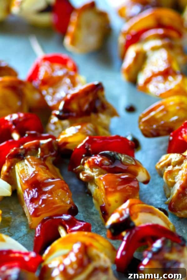 Close-up of a grilled pineapple sweet pepper chicken kebab on a white plate, showcasing the vibrant ingredients and glossy sauce.