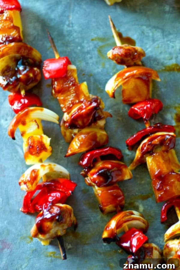 A hand brushing Asian sauce onto pineapple sweet pepper chicken kebabs cooking on a grill.