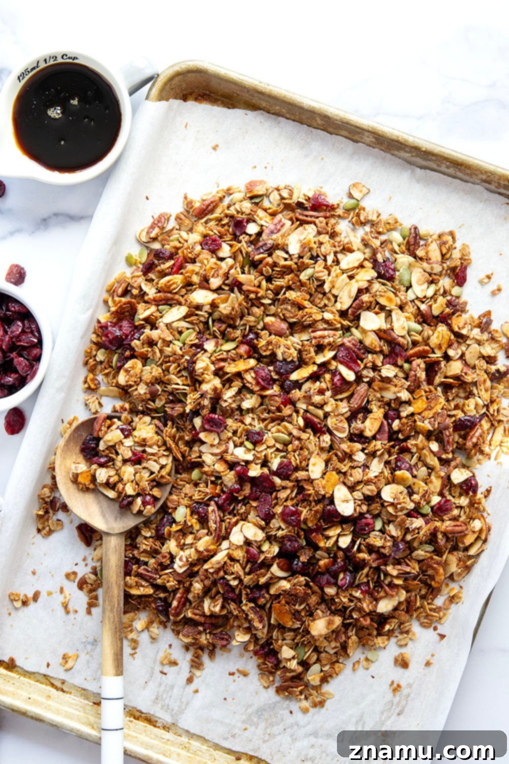 Sweet Maple Crunch 6 A large batch of freshly baked maple granola with nuts and cranberries on a parchment-lined baking sheet.