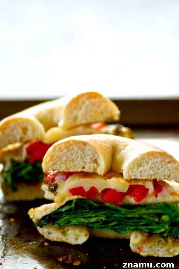 A close-up of a homemade roasted red pepper pesto chicken bagel sandwich, cut in half to reveal its vibrant layers of ingredients, including tender chicken, bright red peppers, and green spinach, all encased in a perfectly toasted bagel.