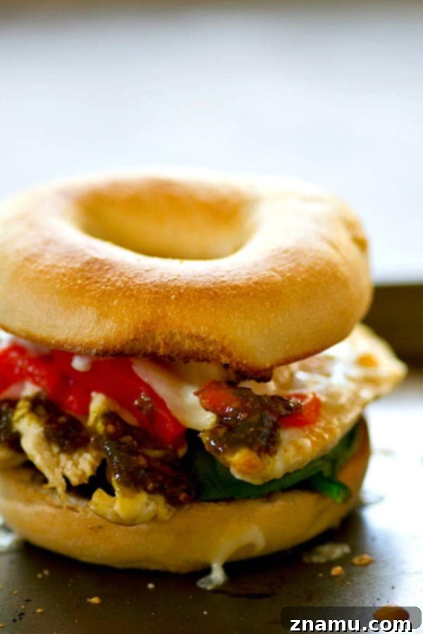 The golden-brown, melted mozzarella cheese bubbling over roasted red peppers and chicken on a toasted bagel half, freshly removed from the broiler. The image captures the inviting warmth and texture of the finished sandwich filling.