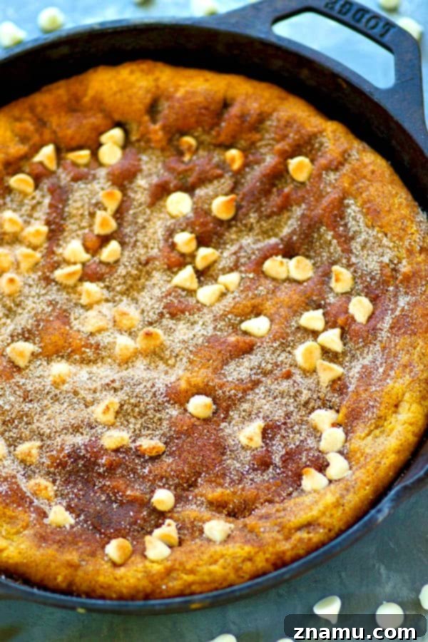 Pumpkin & White Chocolate Snickerdoodle Skillet 5 A slice of white chocolate pumpkin snickerdoodle skillet cookie being carefully removed from the pan, highlighting its gooey texture and white chocolate chunks.