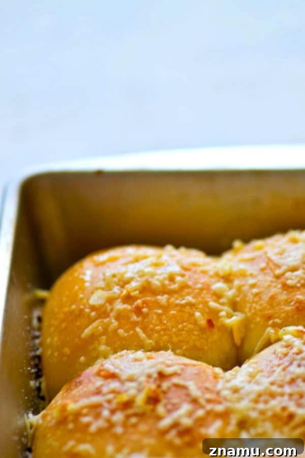 Asiago Roasted Garlic Cornmeal Buns 3 Close-up of a stack of golden brown roasted garlic asiago cornmeal dinner rolls, showcasing their soft texture and melted cheese topping.