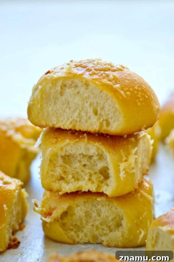Asiago Roasted Garlic Cornmeal Buns 4 A hand reaching for a roasted garlic asiago cornmeal dinner roll, highlighting their fluffy and appealing texture.