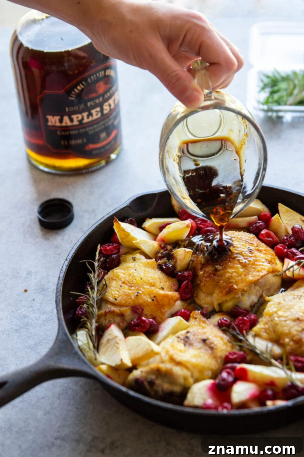 A close-up shot of the maple glazed chicken with cooked cranberries and apples in a skillet.