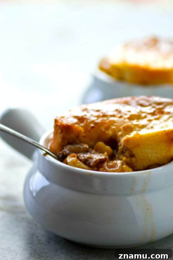 A close-up of a pot of Steak Potato French Onion Soup simmering on the stove, showing the rich broth, onions, steak, and potatoes.