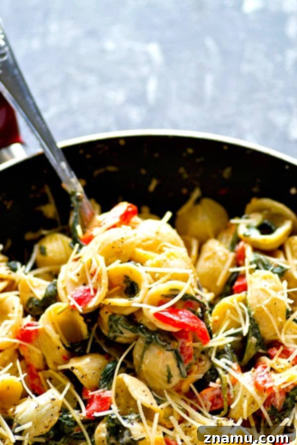 A vibrant close-up of creamy mascarpone orechiette pasta with roasted red peppers and spinach, garnished with fresh parsley.