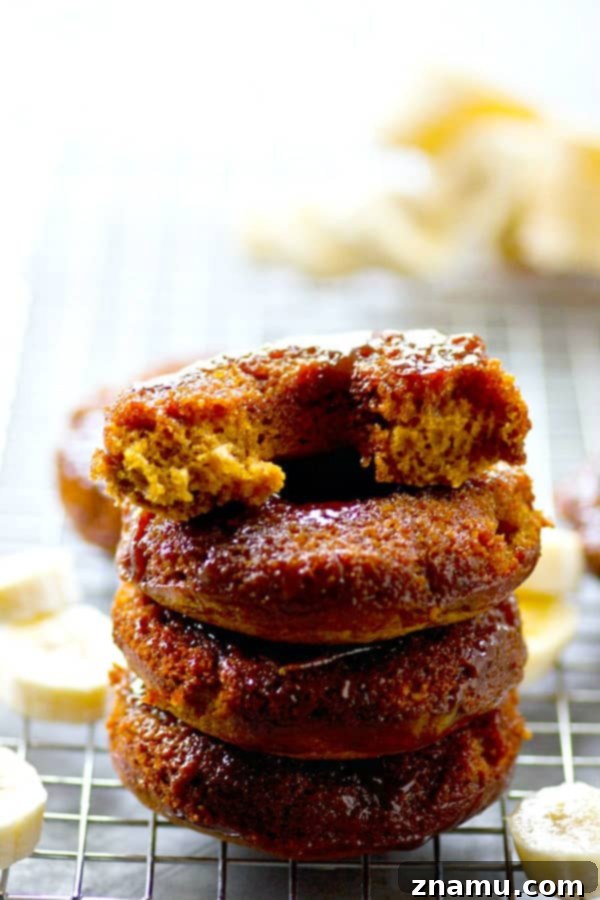 Sticky Caramel Banana Bread Bites 2 A stack of golden-brown banana bread donuts, baked upside-down with shimmering caramel on top, arranged enticingly on a cooling rack.