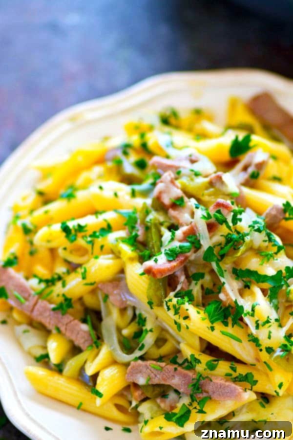 Single-Skillet Philly Cheesesteak Penne 5 Serving of One-Pot Philly Cheesesteak Penne Pasta in a white bowl with a fork, showing melted cheese