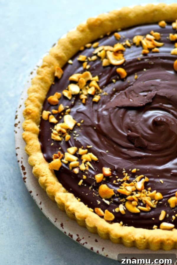 Indulgent Peanut Butter Chocolate Tart 5 A slice of peanut butter cookie chocolate ganache tart garnished with chopped peanuts.