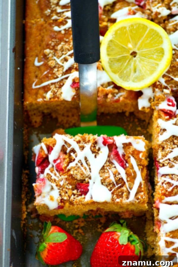 Sunshine Berry Crumb Coffee Cake 3 Close-up of a slice of Strawberry Lemon Crumb Coffee Cake, revealing the moist cake studded with strawberries, a thick crumb topping, and a generous layer of lemon glaze on a rustic wooden surface.