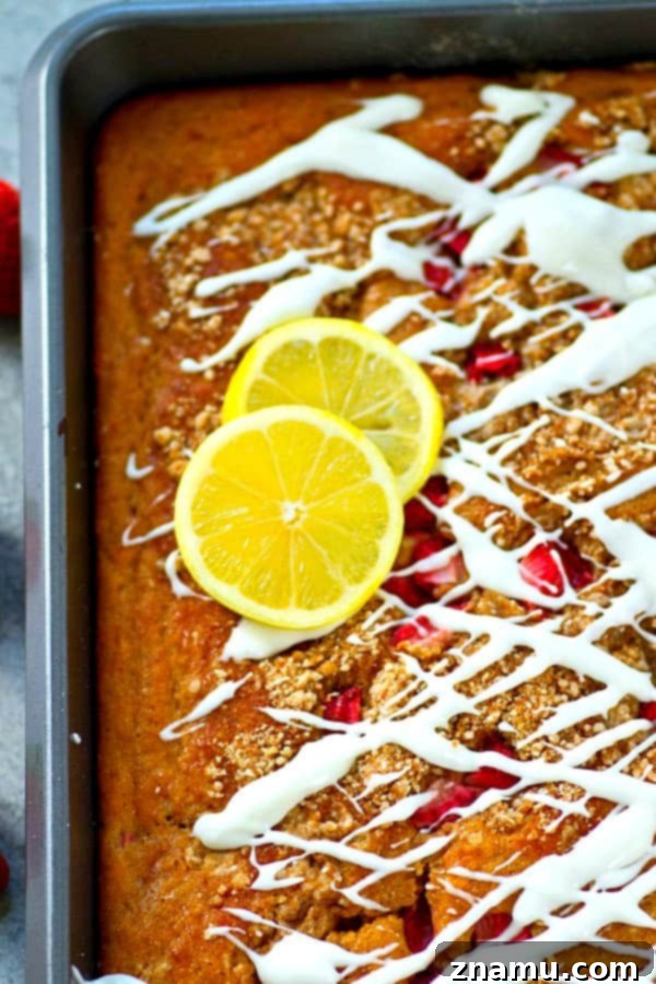 Sunshine Berry Crumb Coffee Cake 5 Overhead shot of a full Strawberry Lemon Crumb Coffee Cake in a baking dish, adorned with fresh strawberry halves and lemon slices, showing its delectable crumb topping and glaze.