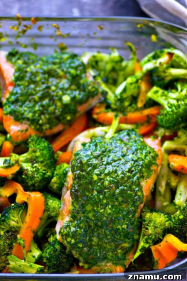 Close-up of freshly baked pesto salmon, glistening with basil pesto, alongside perfectly roasted vegetables