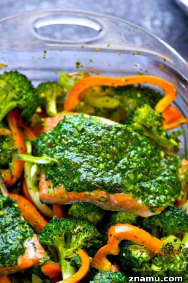 A close-up of a single portion of pesto baked salmon served with roasted broccoli and sweet peppers