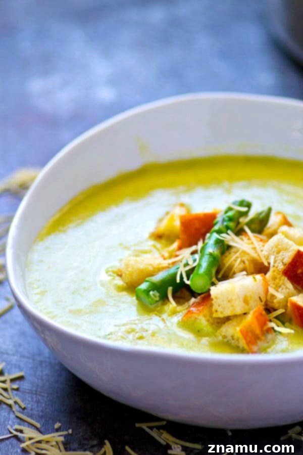 A bowl of asparagus soup garnished with fresh herbs and Parmesan croutons